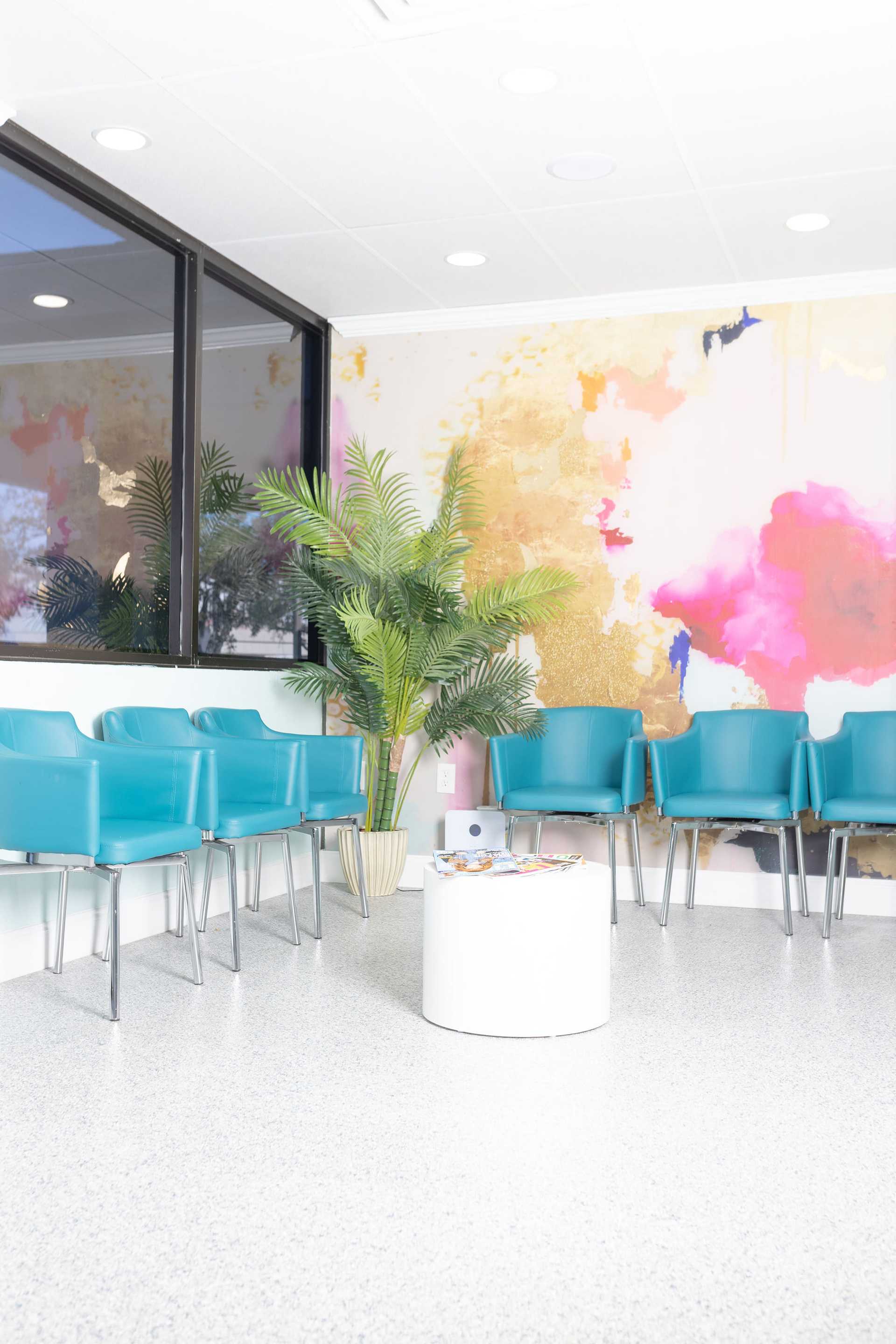 Bright waiting room with blue chairs, a potted plant, and colorful abstract wall art.