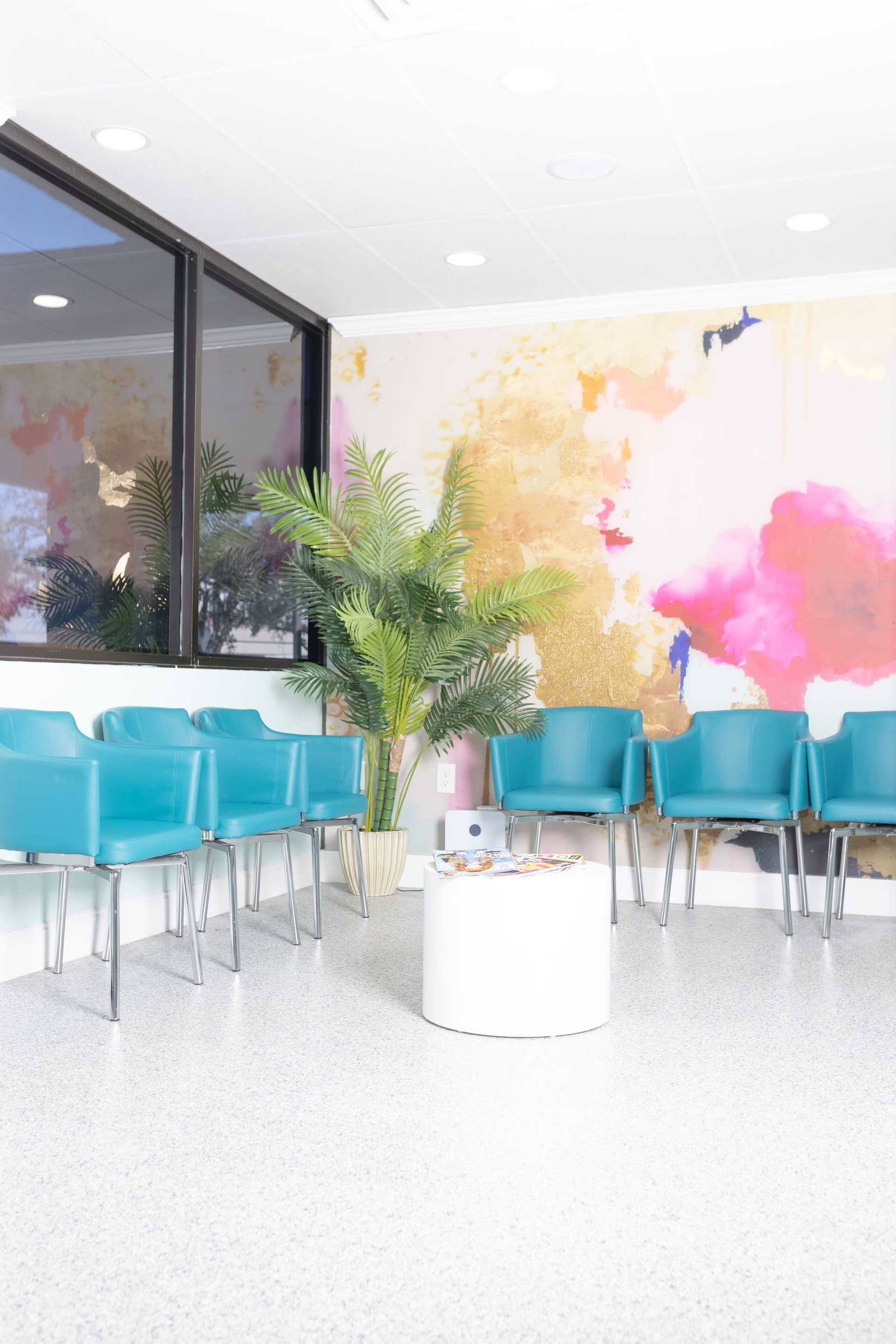 Bright waiting room with blue chairs, a potted plant, and colorful abstract wall art.